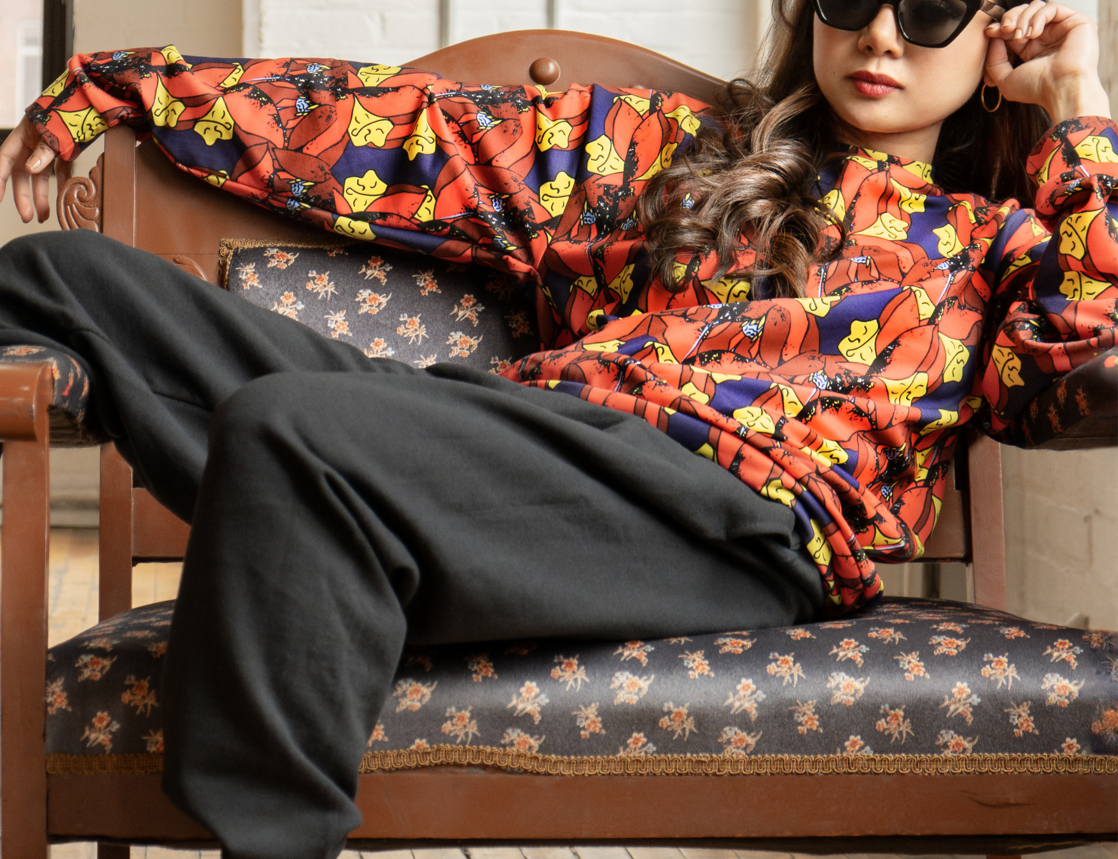 Person wearing a colorful patterned outfit sitting on a floral-patterned chair.