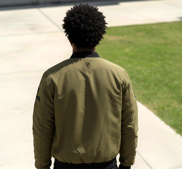 Person wearing a green bomber jacket with a logo on the back, standing on a sidewalk.