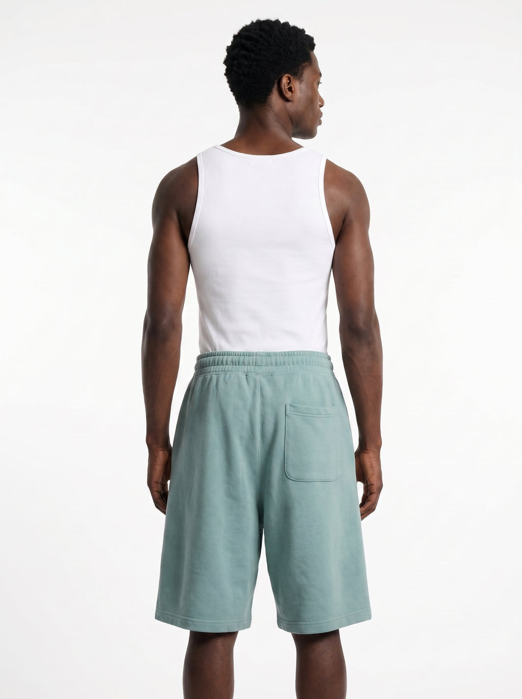 A man shown from the back wearing a white sleeveless tank top and sage green shorts against a plain white studio background.