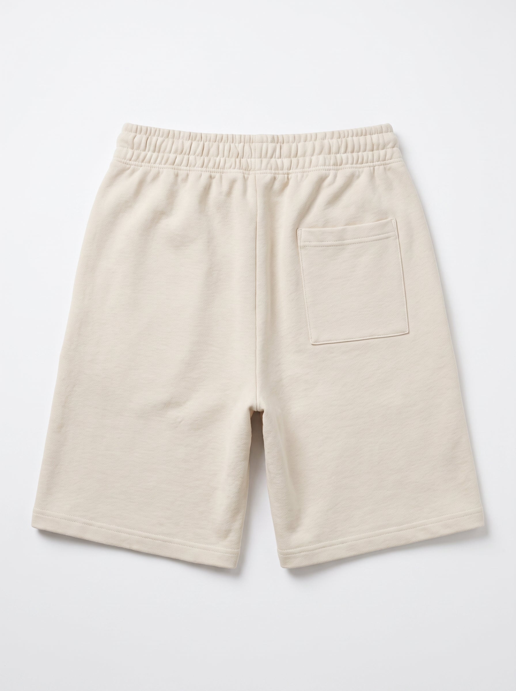 A pair of cream-colored fleece shorts with an elastic waistband and a side pocket, shown from the back on a light gray background.