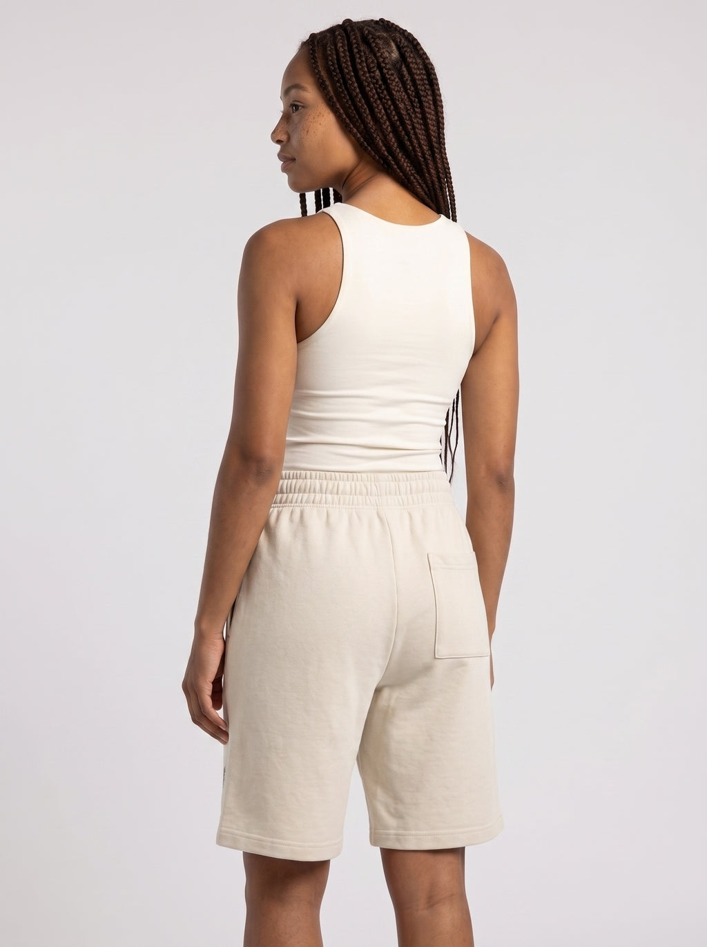 A woman shown from the back wearing a matching off-white ribbed tank top and shorts set against a plain light gray studio background.