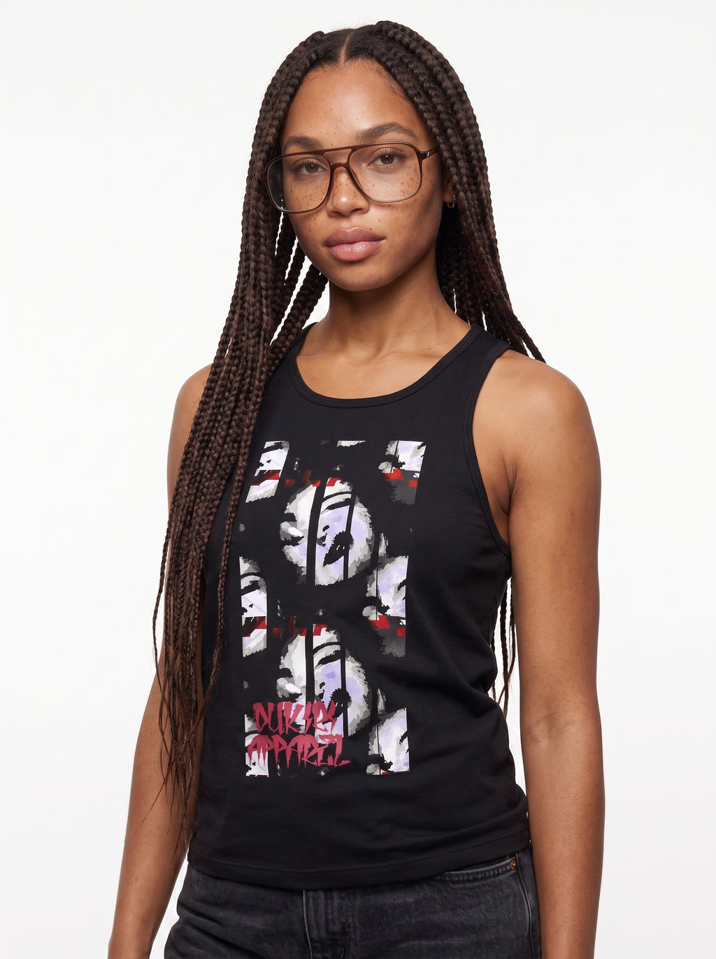 A woman with long dark braids and glasses wearing a black sleeveless tank top with a large white, black, and red graphic print on the front, paired with dark jeans, against a plain white background.