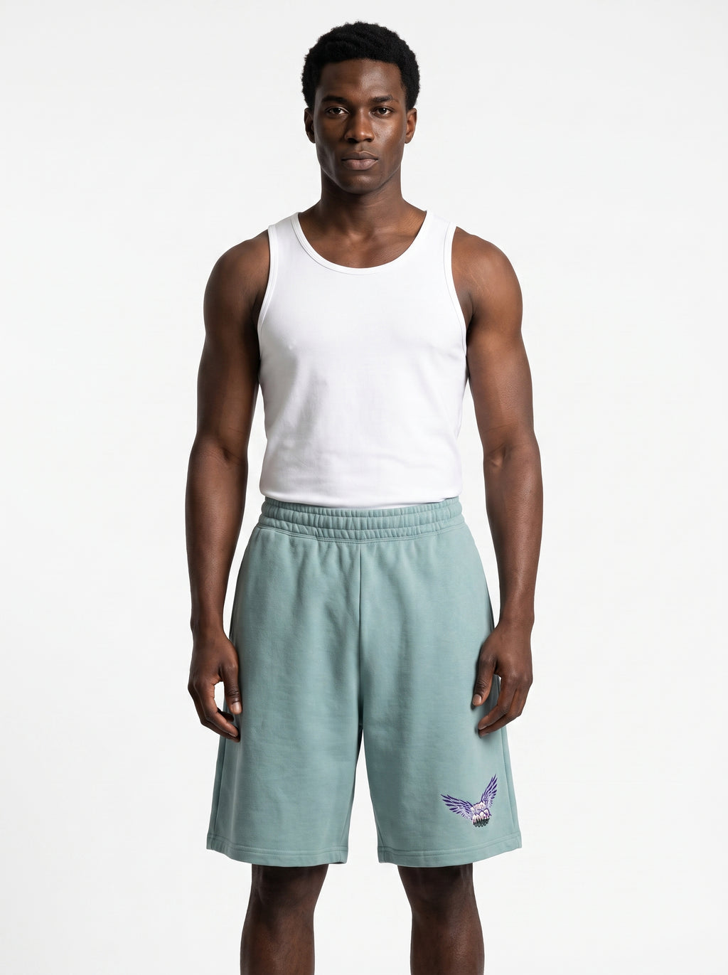 A man modeling a white sleeveless tank top and sage green athletic shorts with a purple and white bird logo on the left leg, set against a plain light gray background.