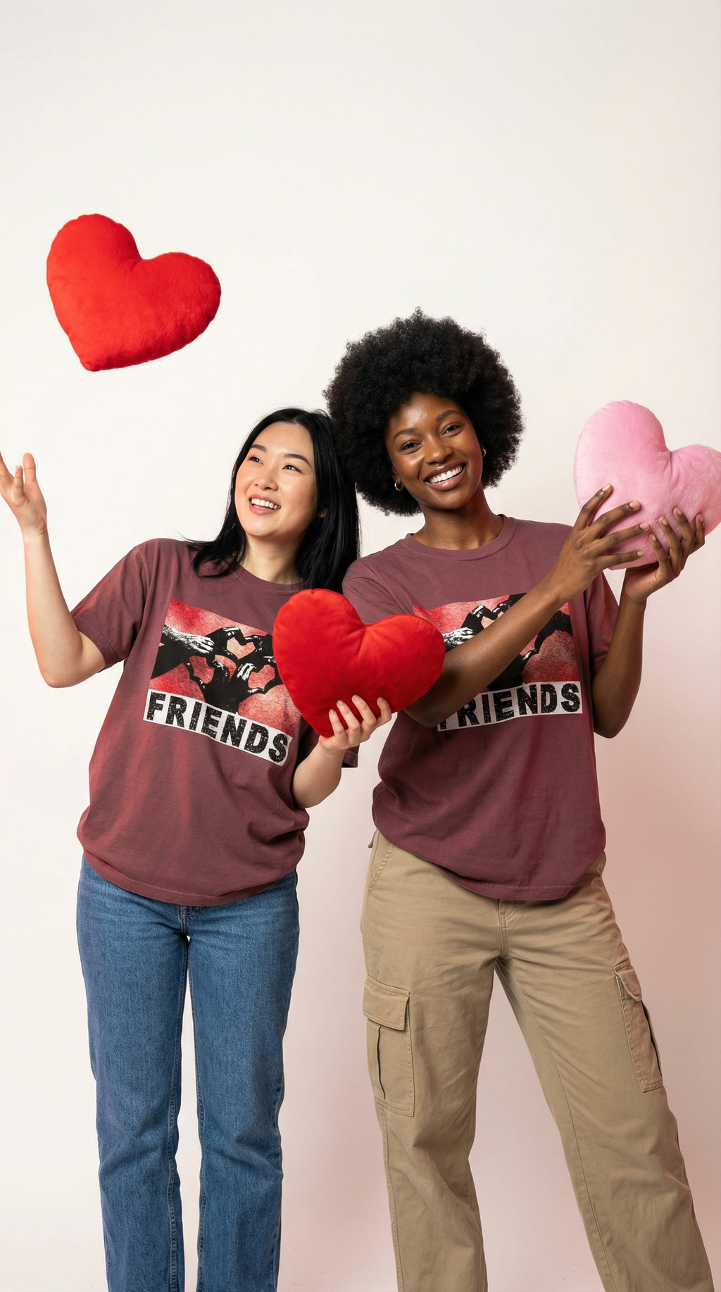 Two people wearing 'Friends' t-shirts holding heart-shaped props against a plain background