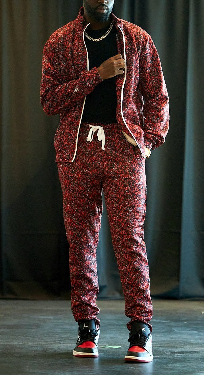 Person wearing a red patterned tracksuit against a dark curtain background